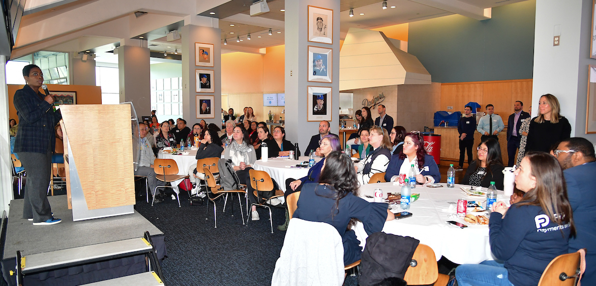Nichol Whiteman, LA Dodgers Foundation CEO holding a microphone and speaking to a large audience in the Stadium Club